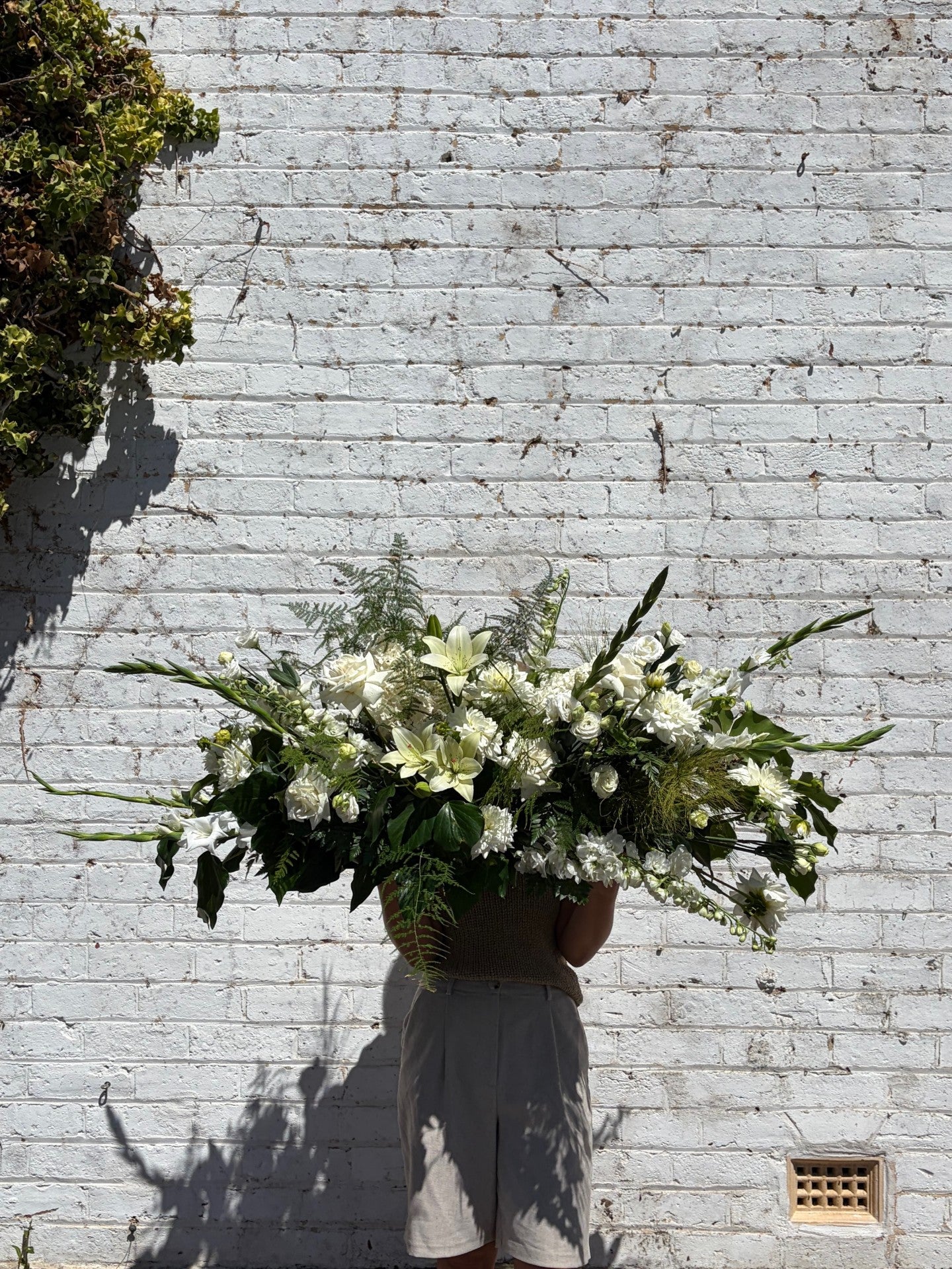 Person holding a large floral arrangement against a light brick wall.