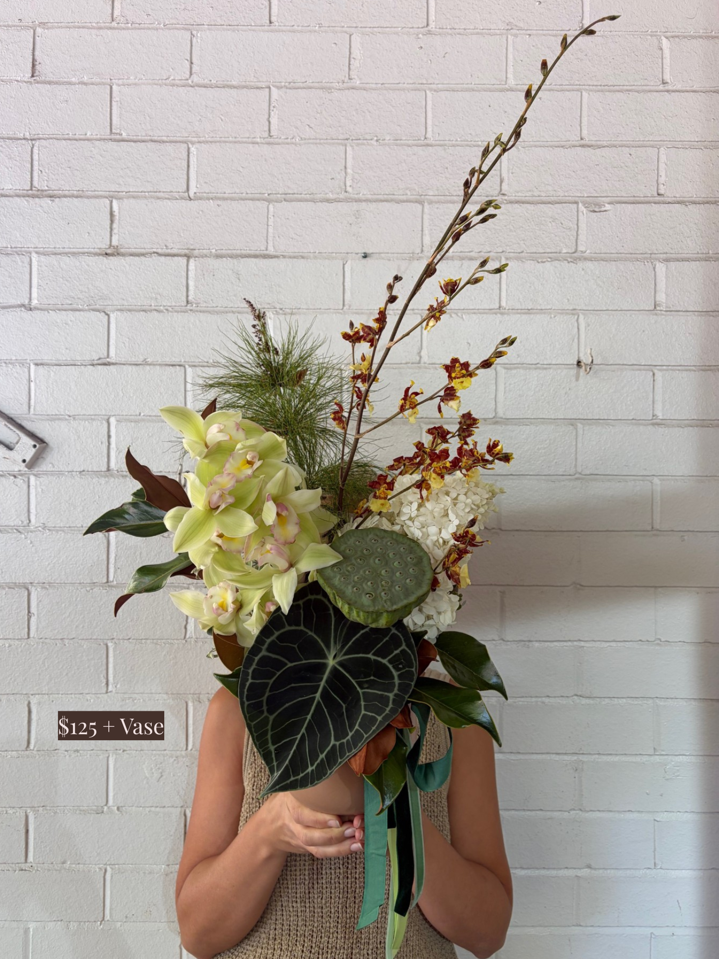 Person holding a bouquet of flowers against a white brick wall
