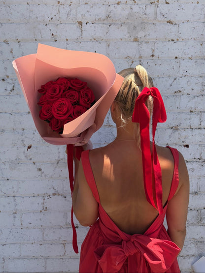 Woman in a red dress holding a large bouquet of red roses against a white brick wall.