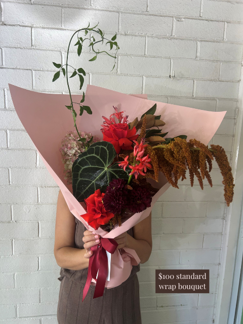 Bouquet of flowers held by a person against a white brick wall with a price label.