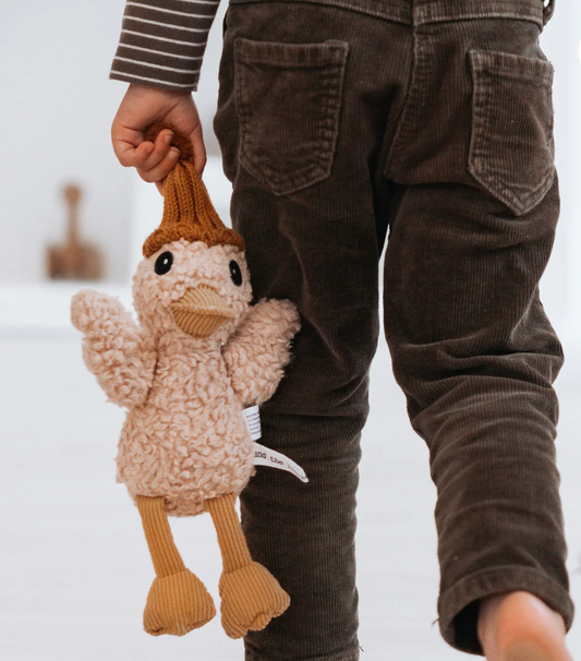 Child holding a knitted toy duck with brown pants on a white background