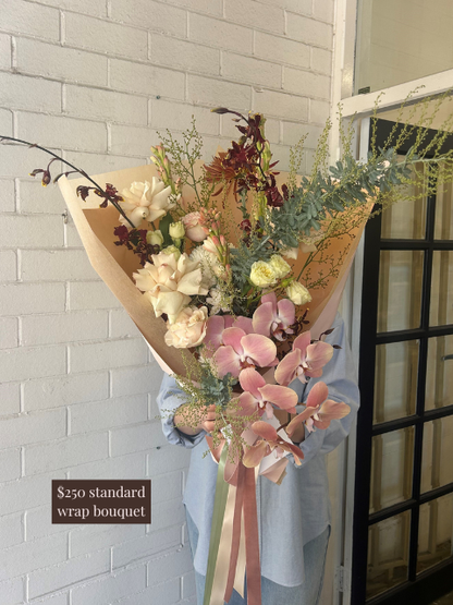 Bouquet of flowers wrapped in brown paper with a price tag in front of a white brick wall.