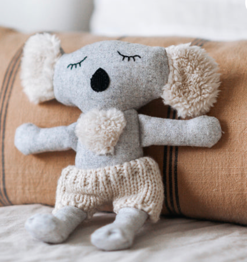 Plush toy koala in a knitted outfit sitting on a couch