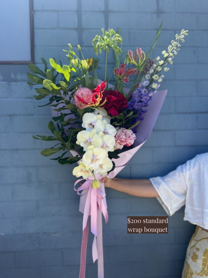 Bouquet of flowers with a pink ribbon held against a blue wall.