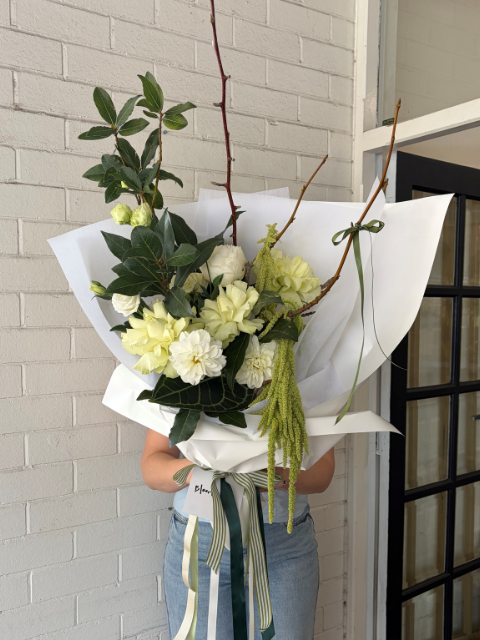 Bouquet of flowers wrapped in white paper held by a person against a light brick wall.