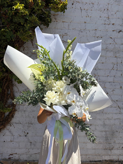 Bouquet of flowers wrapped in white paper against a textured wall.