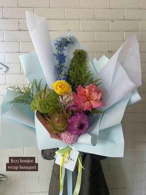 Bouquet of flowers wrapped in light blue paper against a tiled wall.