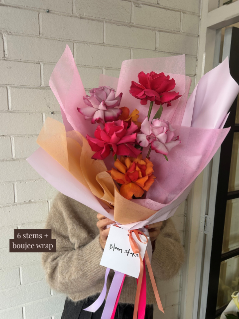 Bouquet of flowers with colorful paper wrapping held by a person against a white brick wall.