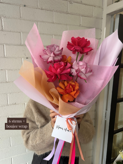 Bouquet of flowers with colorful paper wrapping held by a person against a white brick wall.