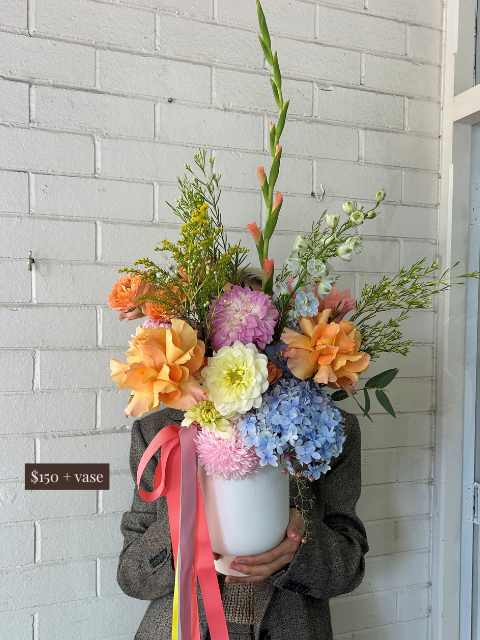 Person holding a colorful bouquet of flowers against a light gray brick wall.