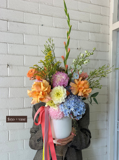 Person holding a colorful bouquet of flowers against a light gray brick wall.