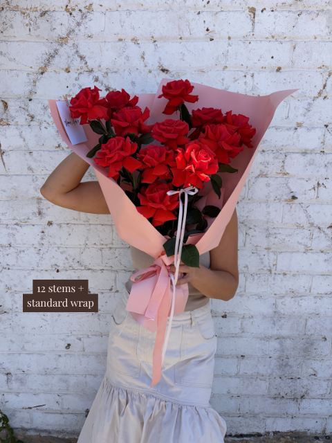 Person holding a bouquet of red roses against a white brick wall