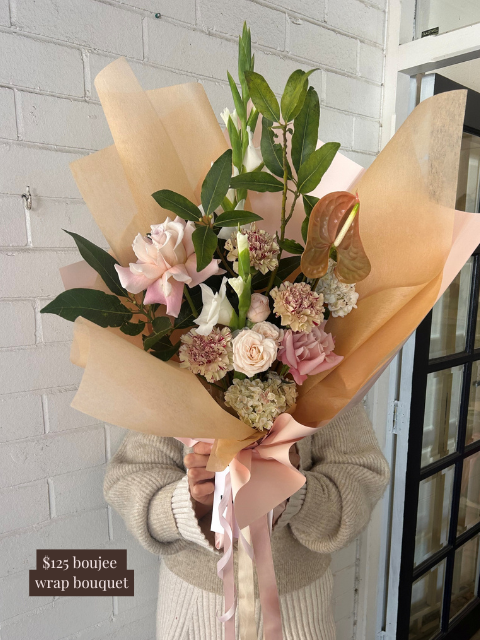 Bouquet of flowers wrapped in brown paper held by a person against a white brick wall.