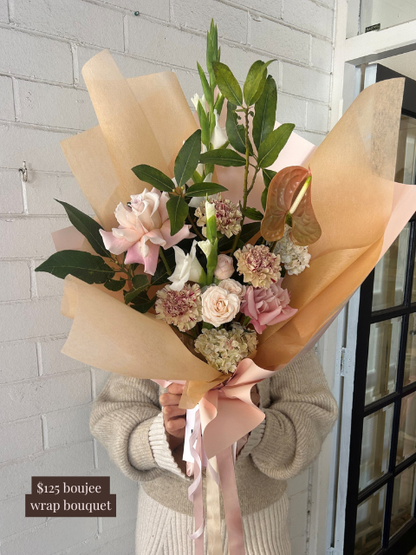 Bouquet of flowers wrapped in brown paper held by a person against a white brick wall.