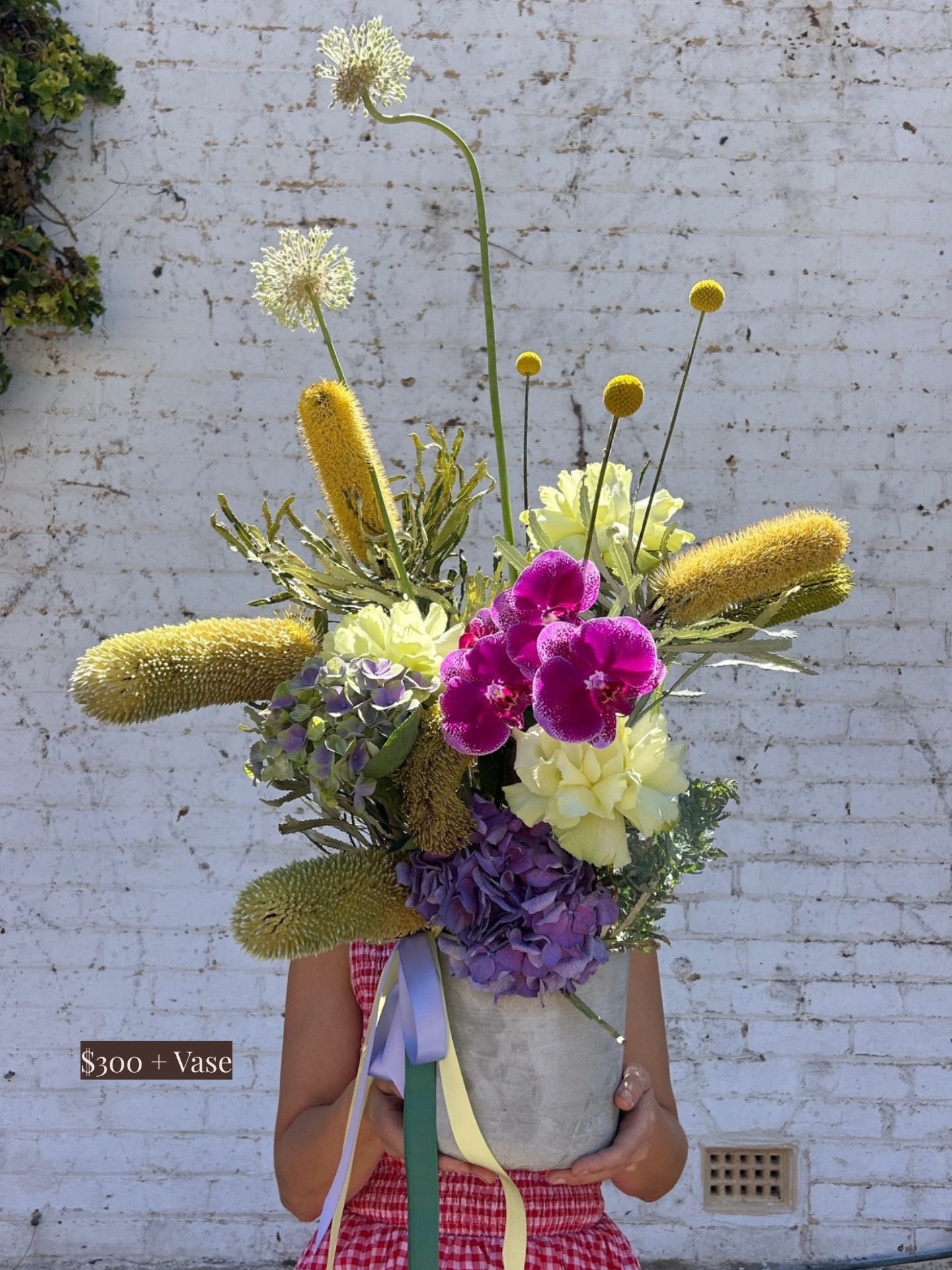 Person holding a colourful vase arrangement against a white brick wall