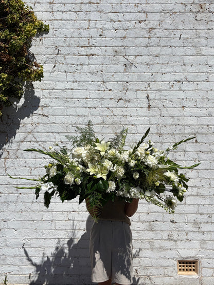 Person holding a large floral arrangement against a light brick wall.