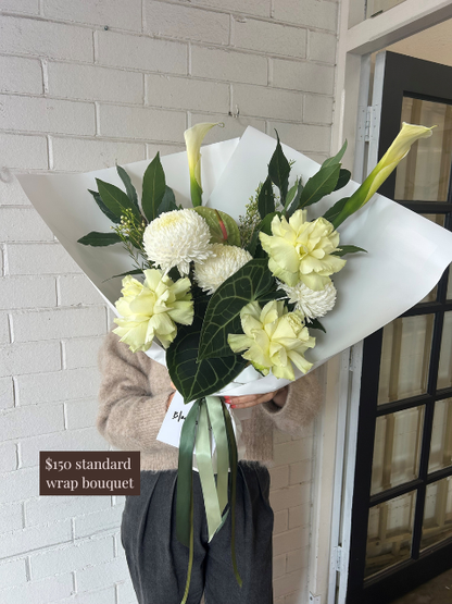 Bouquet of white flowers with green leaves held by a person against a light-colored wall.
