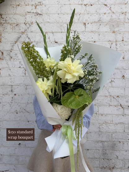 Bouquet of flowers wrapped in paper against a white brick wall.