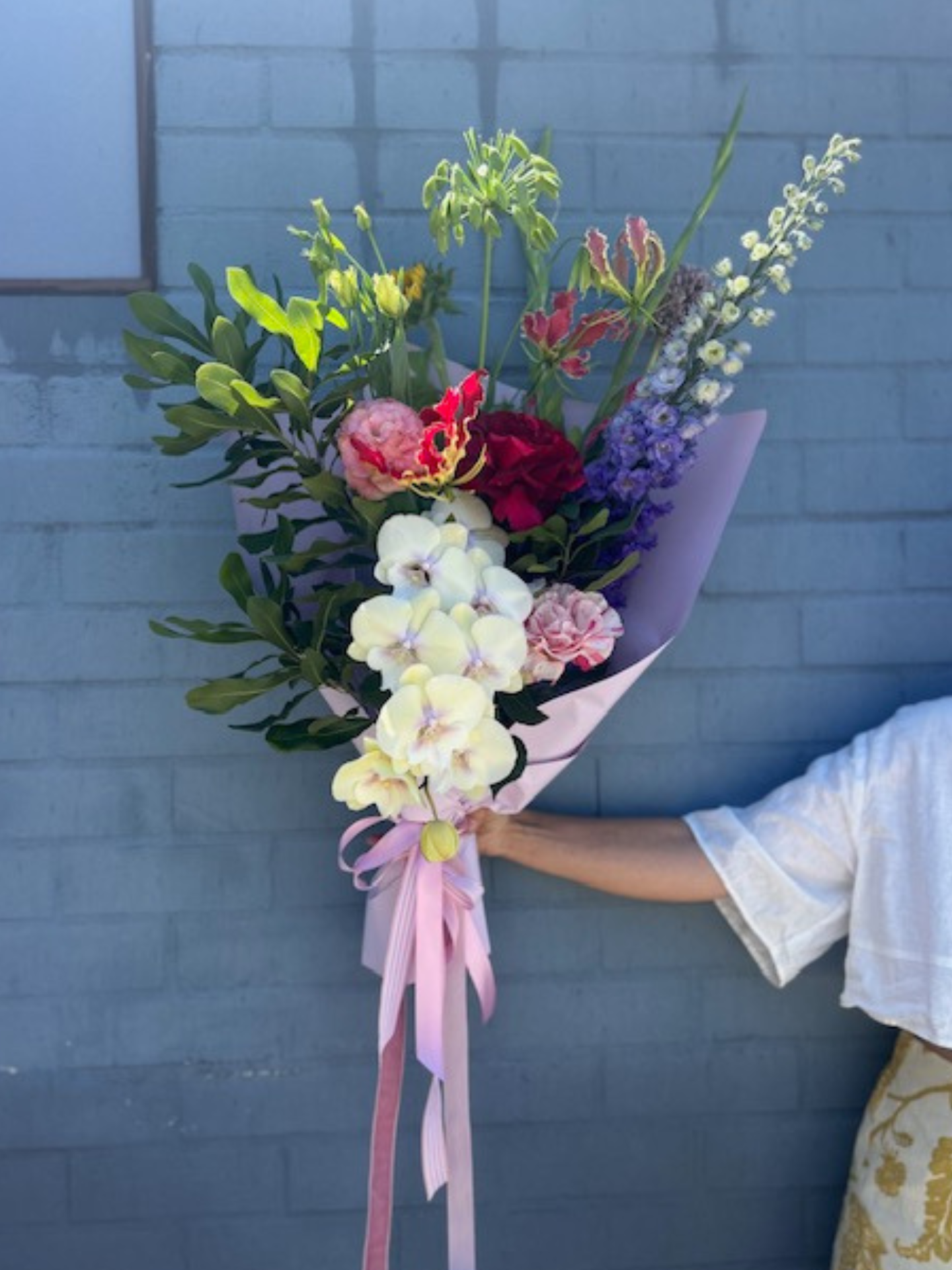 Bouquet of colourful flowers held by a person against a blue brick wall