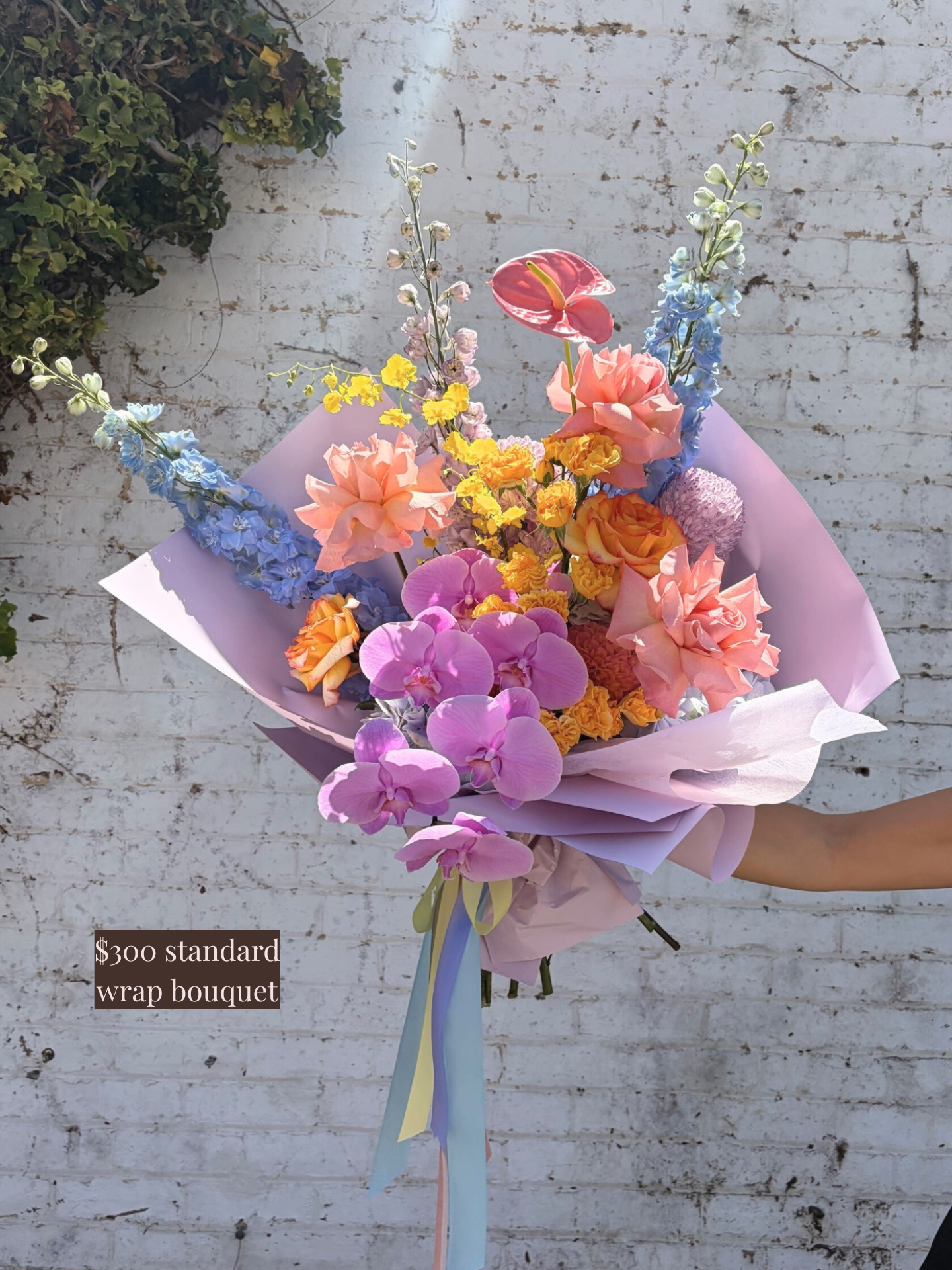 Colorful bouquet of flowers with a pink wrap against a white brick wall.