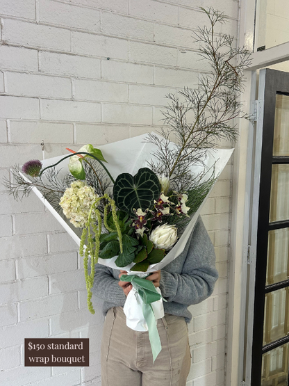 Person holding a bouquet of flowers against a light brick wall.