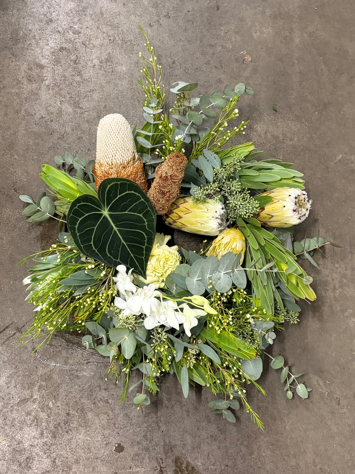 Floral wreath arrangement with greenery and white flowers on a concrete surface