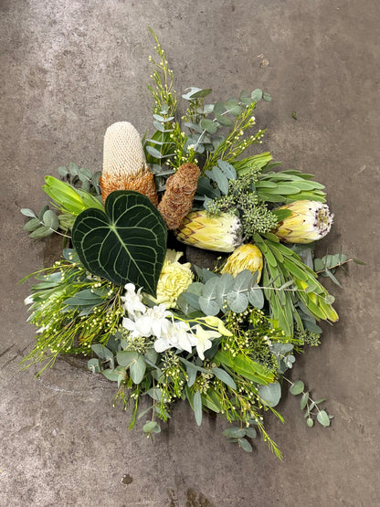 Floral wreath arrangement with greenery and white flowers on a concrete surface