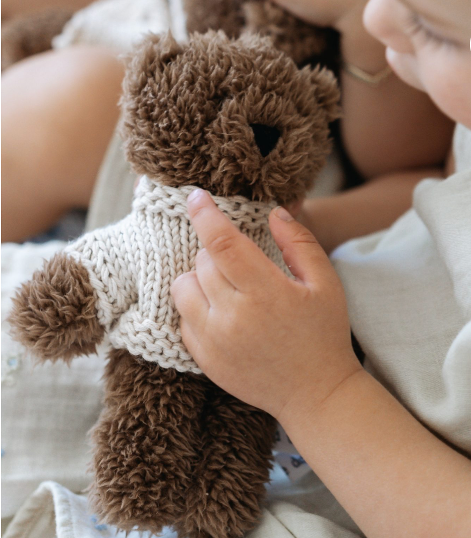 Child holding a brown teddy bear with a knitted sweater