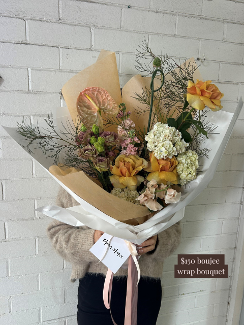Bouquet of flowers wrapped in brown paper with a price tag against a white brick wall.