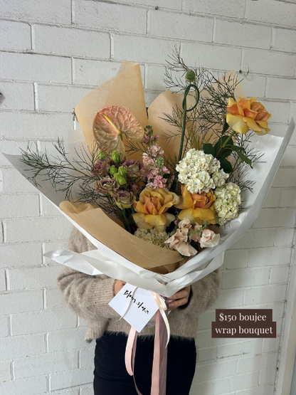 Bouquet of flowers wrapped in brown paper with a price tag against a white brick wall.