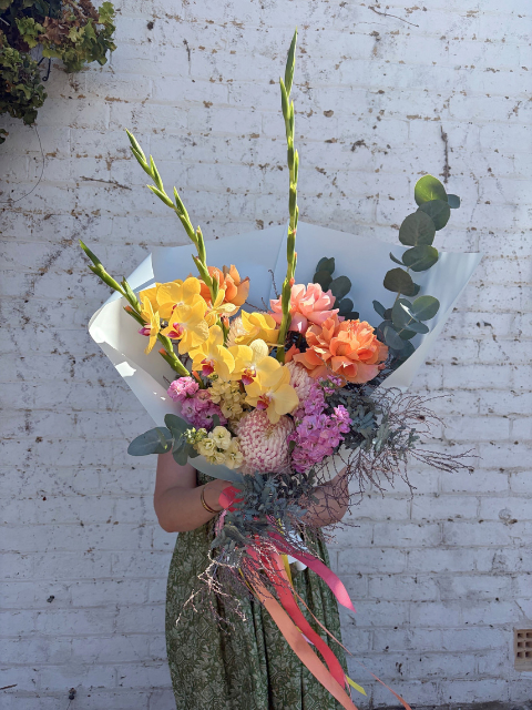 Bouquet of flowers held by a person against a white brick wall.