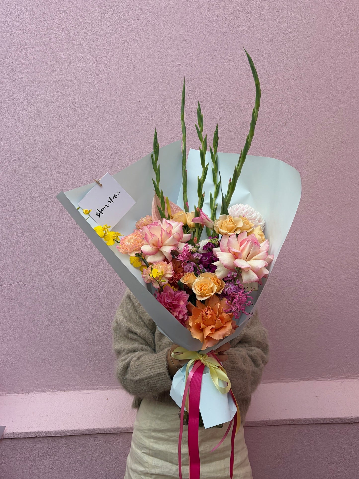 Person holding a bouquet of flowers against a pink wall
