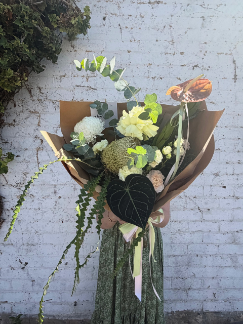 Bouquet of flowers wrapped in brown paper against a white brick wall.