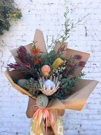 Bouquet of flowers wrapped in brown paper with a white brick background
