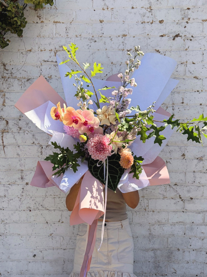 Bouquet of flowers wrapped in white paper with pink ribbons against a white brick wall.
