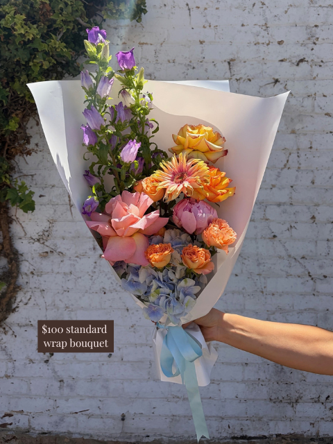 Bouquet of flowers held by a person against a white brick wall.