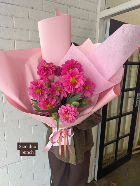 Bouquet of pink flowers wrapped in pink paper with a price tag on a white brick wall background.
