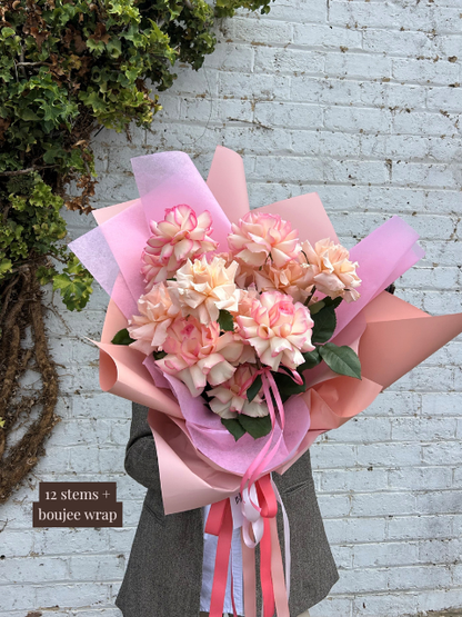 Bouquet of pink flowers with a pink wrap held against a white brick wall.