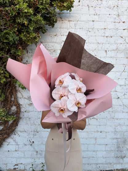 Bouquet of pink flowers with brown ribbons held by a person against a white brick wall.
