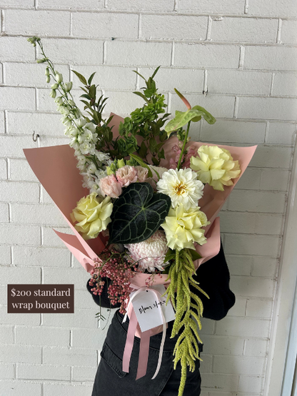 Bouquet of flowers wrapped in pink paper against a white brick wall.