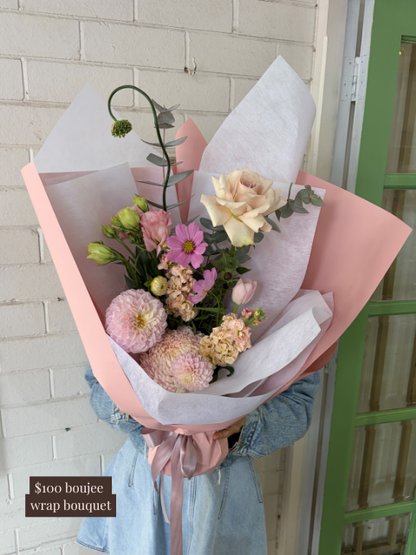 Bouquet of flowers wrapped in pink paper held by a person wearing a denim jacket.