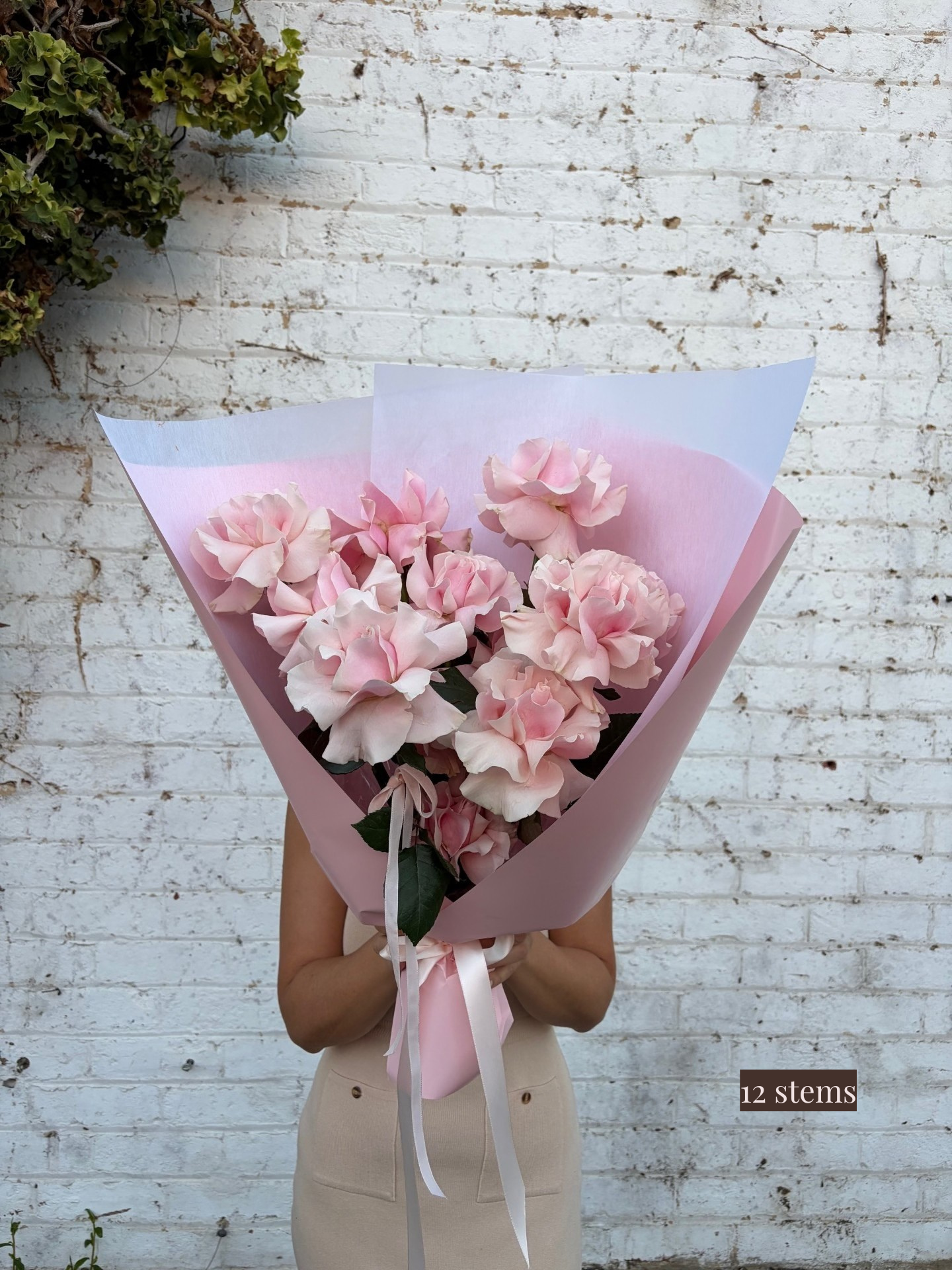 Bouquet of pink flowers held by a person against a white brick wall.