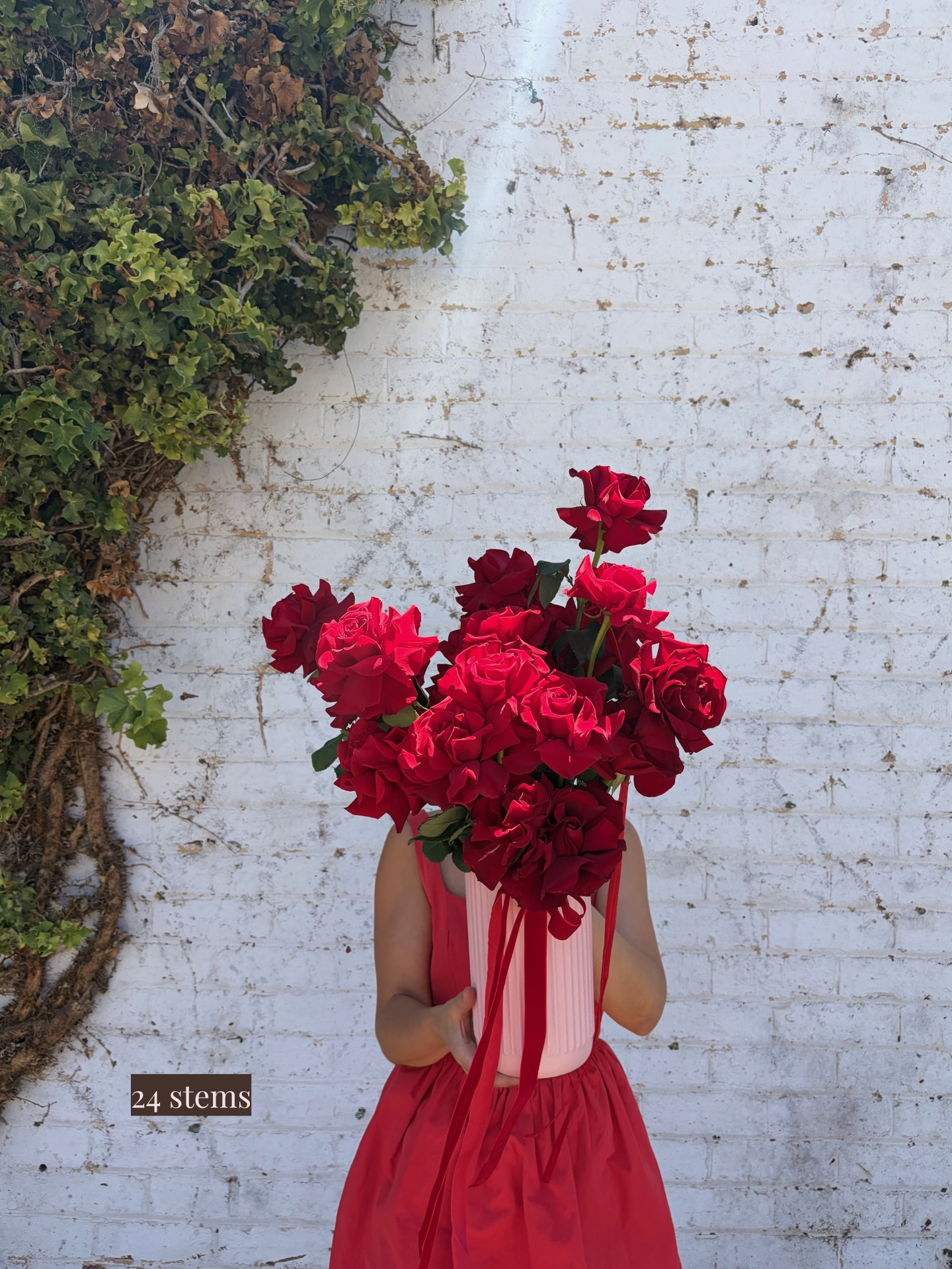 Person holding a large bouquet of red roses against a white brick wall.