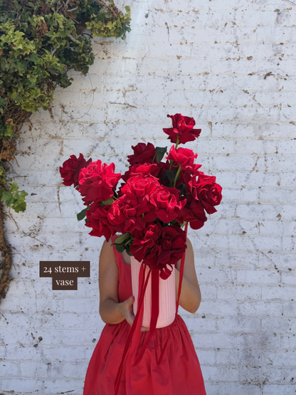 Person holding a large bouquet of red flowers against a white brick wall.