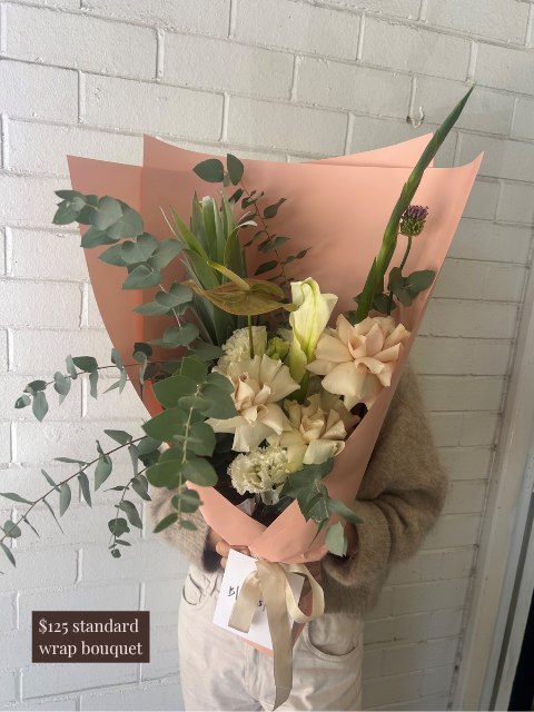 Bouquet of flowers wrapped in pink paper held against a white brick wall.