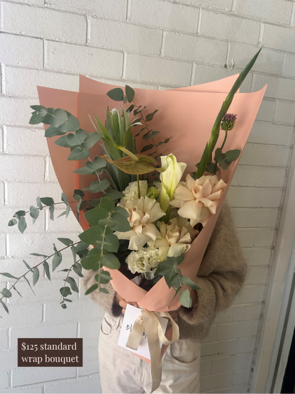 Bouquet of flowers wrapped in pink paper held against a white brick wall.