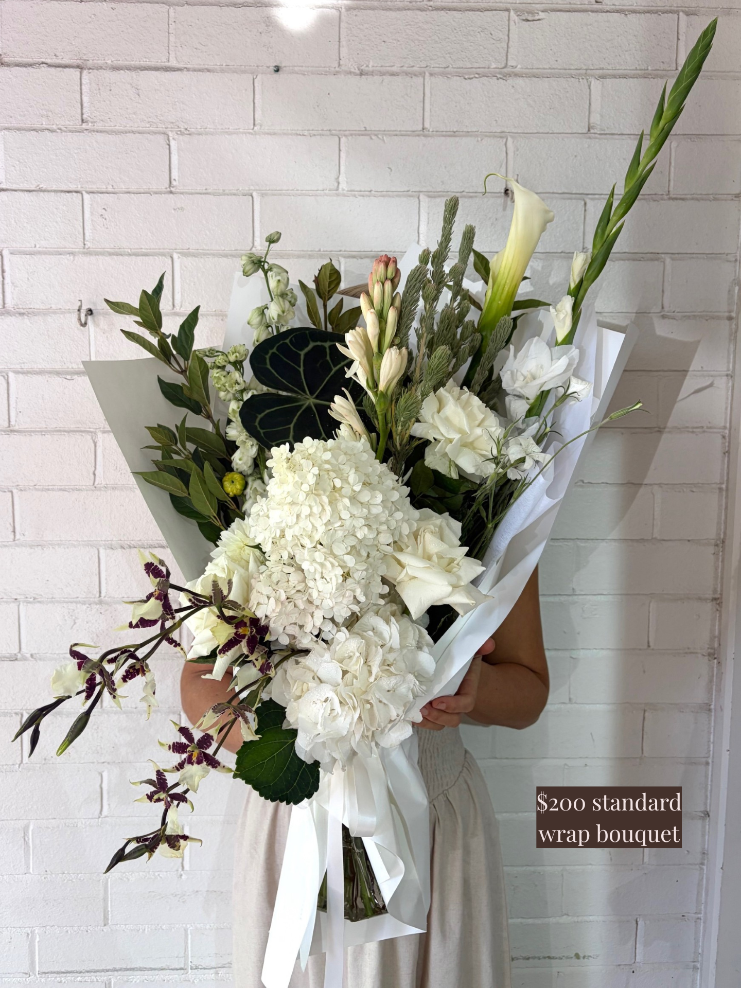 Bouquet of flowers held against a white brick wall with a price tag overlay.