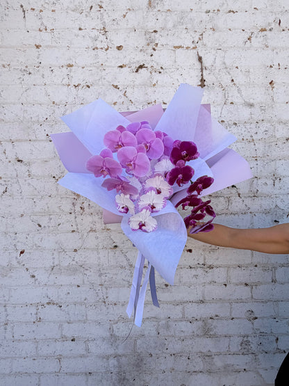 Bouquet of purple and white orchid flowers held by a person on a textured surface