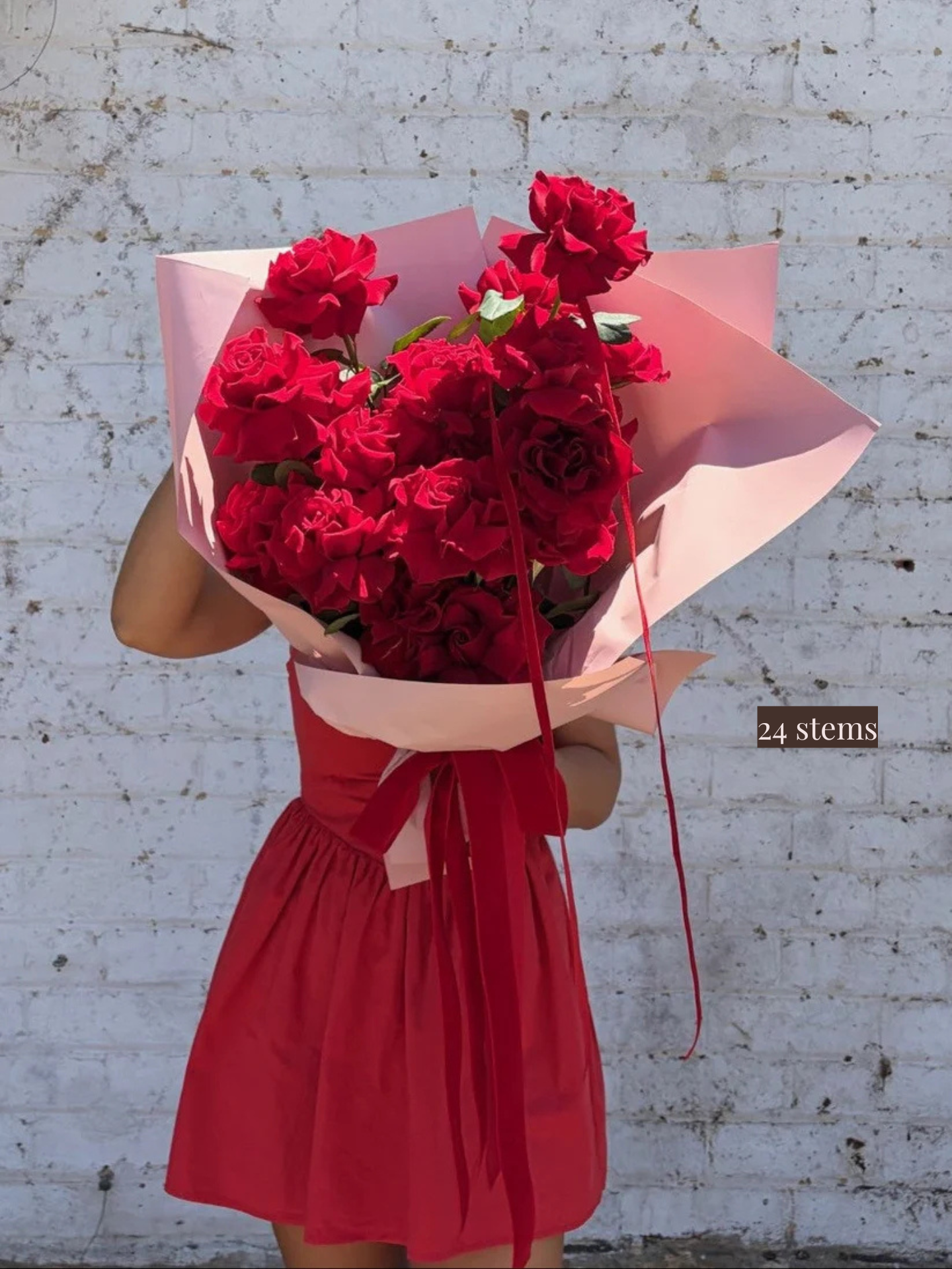Person holding a bunch of red roses wrapped in pink paper.
