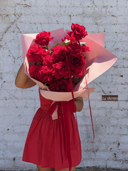 Person holding a bunch of red roses wrapped in pink paper.